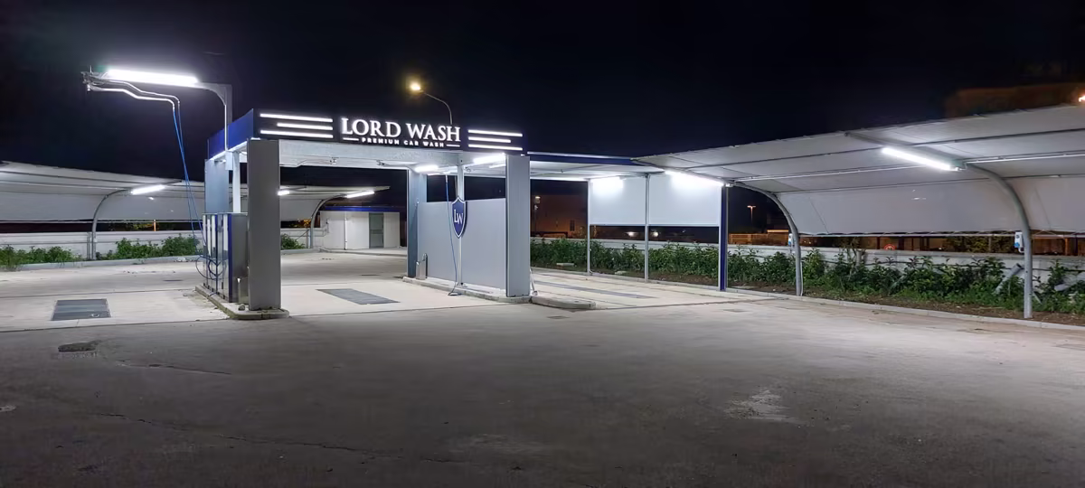 Vista d'insieme di sera dell'autolavaggio Lord Wash con l'ingresso illuminato e le piste coperte da tettoie